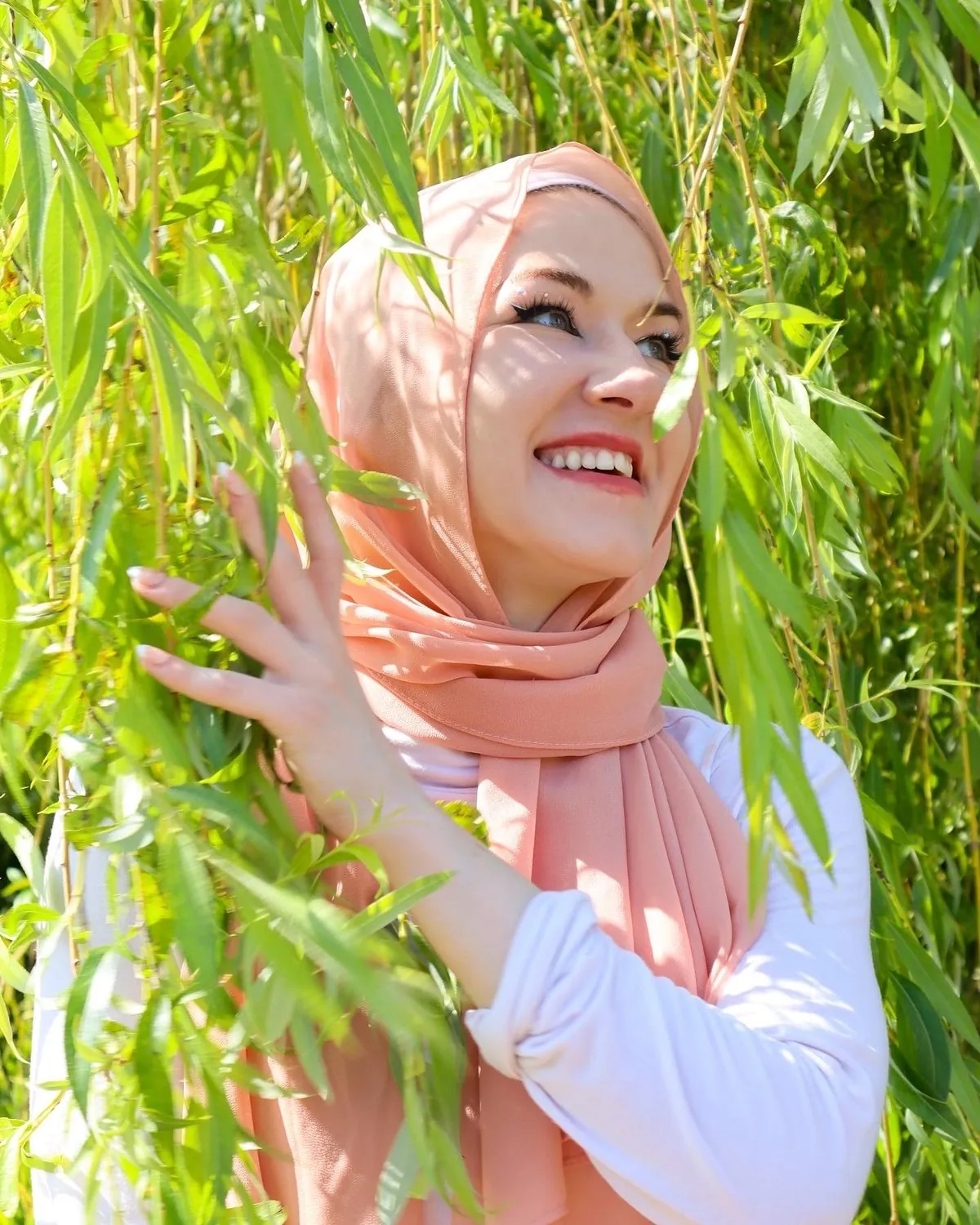 Agne Ajauskaite smiling among the leaves of a willow tree.